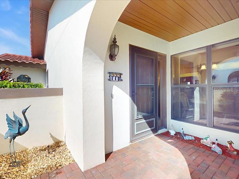A covered brick entryway features a dark front door, a wall-mounted lantern, and decorative figurines — 118 COVENTRY LANE, HAINES CITY, FL