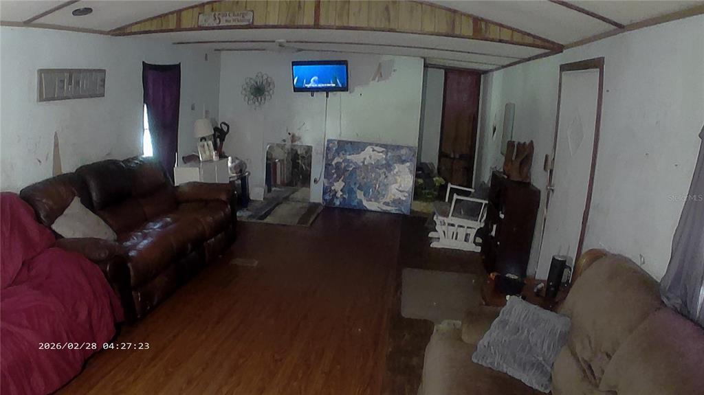 A living room features wood-look flooring, two sofas, a wall-mounted television, and wood-paneled ceiling trim — 16979 SE 6TH LANE, SILVER SPRINGS, FL