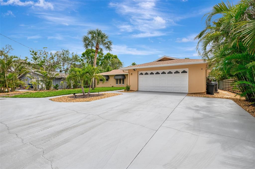 A tan single-story house with a white two-car garage and a large concrete driveway — 4946 COMMONWEALTH DRIVE, SARASOTA, FL
