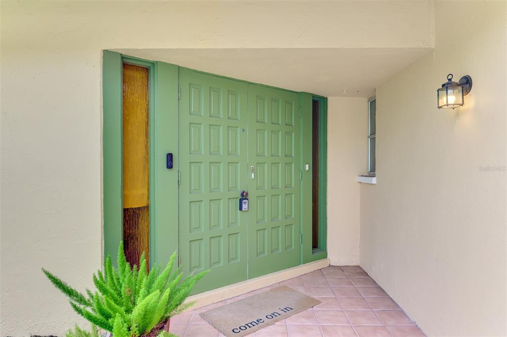 A green double front door with sidelights sits under a covered entryway with tiled flooring — 4946 COMMONWEALTH DRIVE, SARASOTA, FL