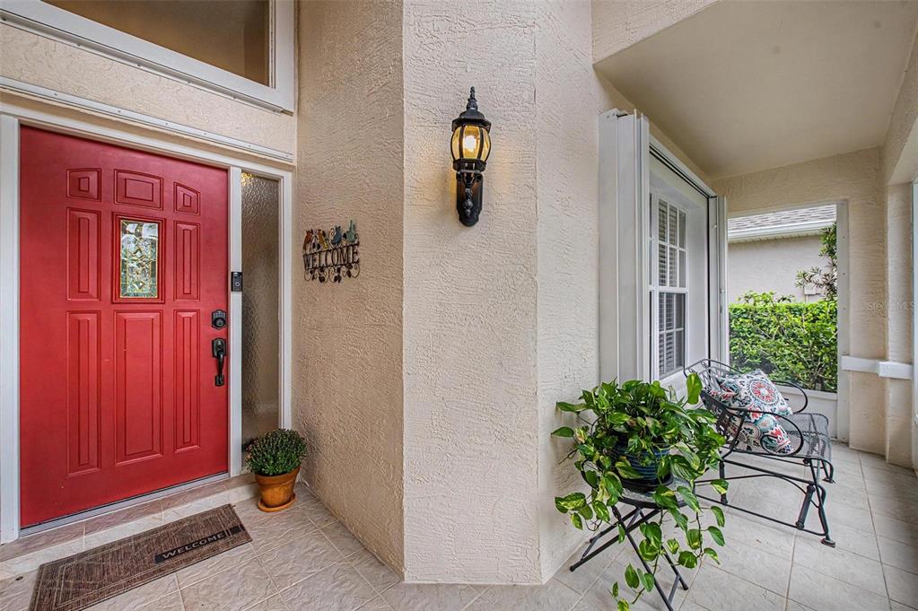 A red front door with a sidelight and a covered porch with a potted plant — 1808 ORCHARDGROVE AVENUE, NEW PORT RICHEY, FL