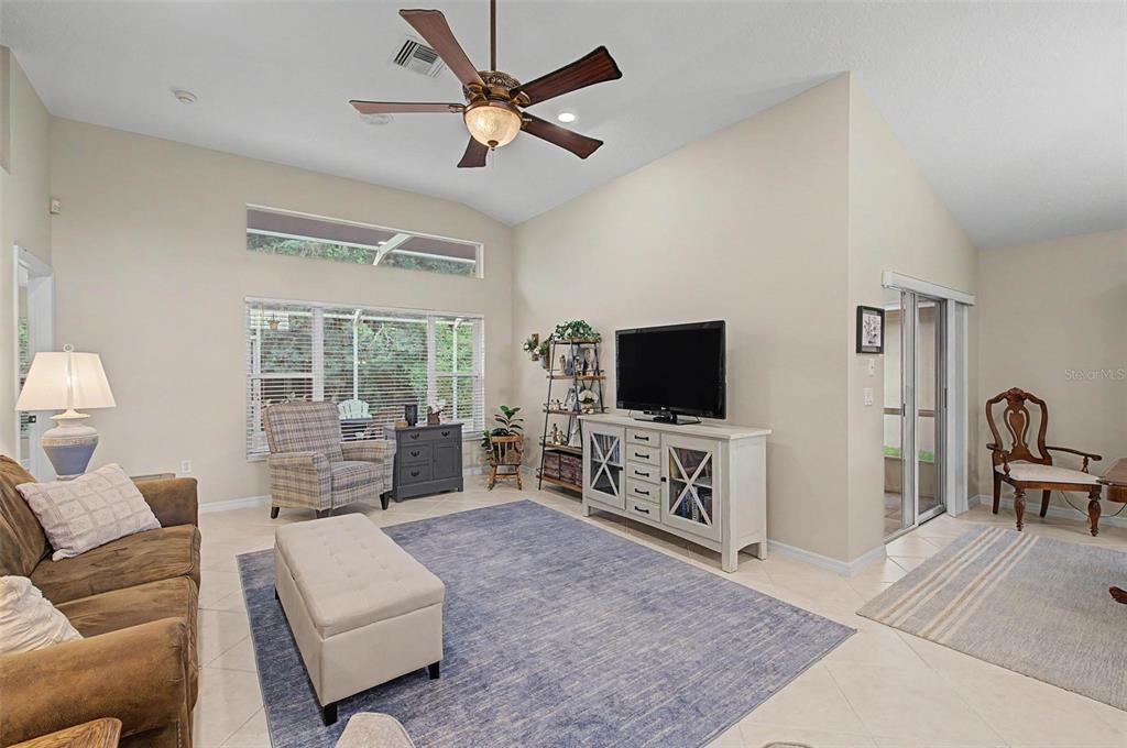 A living room features a vaulted ceiling, a ceiling fan, tile flooring, and a television console — 1808 ORCHARDGROVE AVENUE, NEW PORT RICHEY, FL