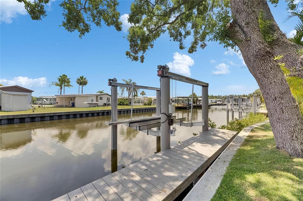 A wooden dock features a boat lift extending over a canal near residential homes — 6532 SIMONE SHORES CIRCLE, APOLLO BEACH, FL