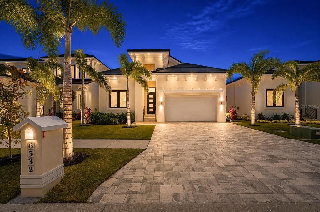 A modern single-story house with a paved driveway, palm trees, and a lit exterior at dusk — 6532 SIMONE SHORES CIRCLE, APOLLO BEACH, FL