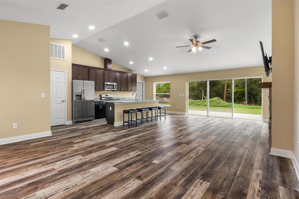 An open-concept kitchen and living area features dark wood cabinets, stainless appliances, and wood-look flooring — 6929 WILBAR LANE, HAINES CITY, FL