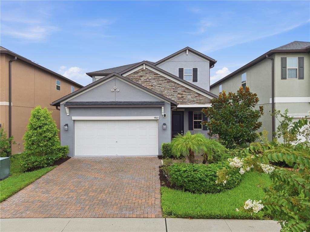 A two-story suburban house with a gray stucco exterior, stone accents, and a paved driveway — 9807 WILD BEGONIA LOOP, LAND O LAKES, FL
