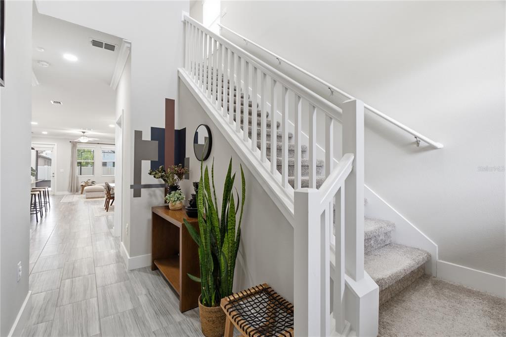 A carpeted staircase with a white railing sits beside a wooden console table and plant — 9807 WILD BEGONIA LOOP, LAND O LAKES, FL