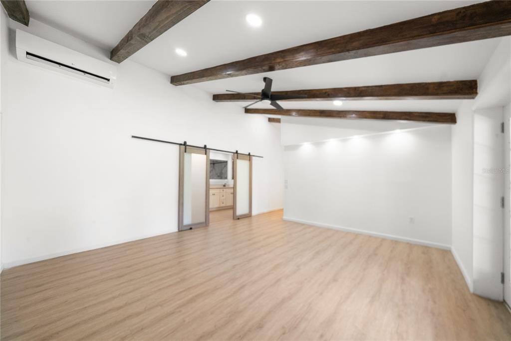 A room with light wood floors, white walls, exposed ceiling beams, and sliding barn doors — 19520 168TH STREET, LIVE OAK, FL