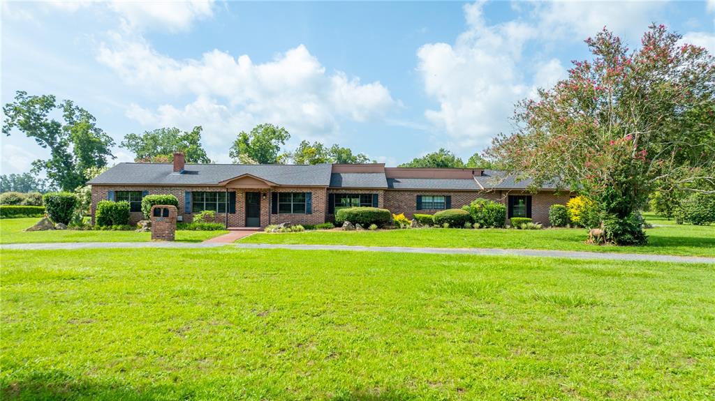 A single-story brick house with a dark shingled roof sits on a large grassy lawn — 19520 168TH STREET, LIVE OAK, FL