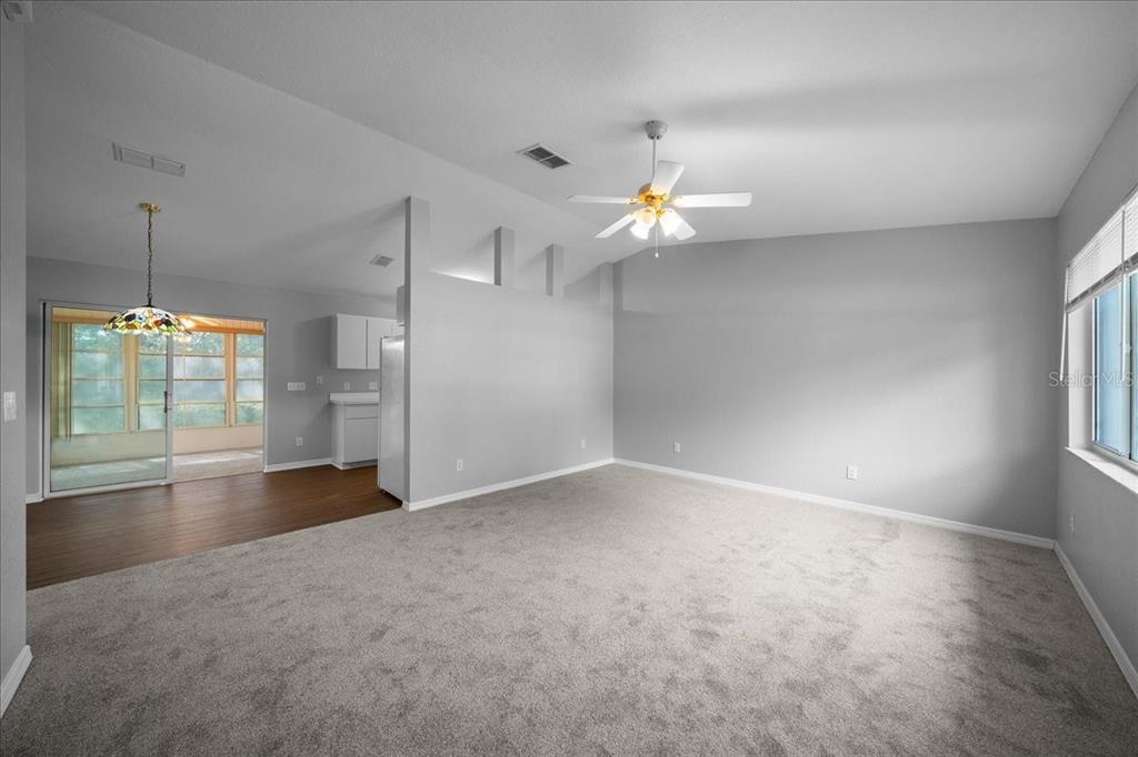 A living room with gray carpet and walls, a ceiling fan, and an adjacent kitchen area — 9912 SW 61ST COURT, OCALA, FL