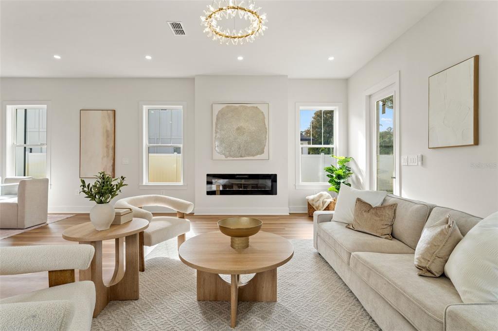 A bright living room features a fireplace, neutral furniture, and a modern chandelier — 10164 HODSON PLACE, SEMINOLE, FL