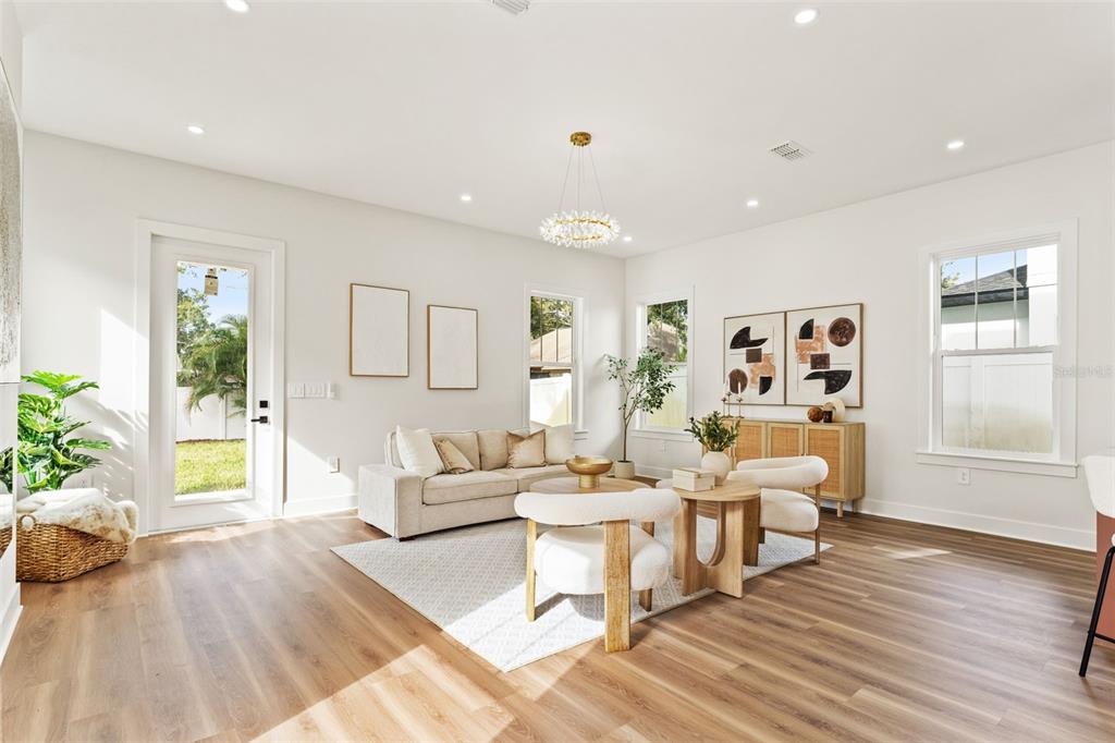 A bright living room features light wood flooring, a beige sofa, and two round chairs — 10164 HODSON PLACE, SEMINOLE, FL