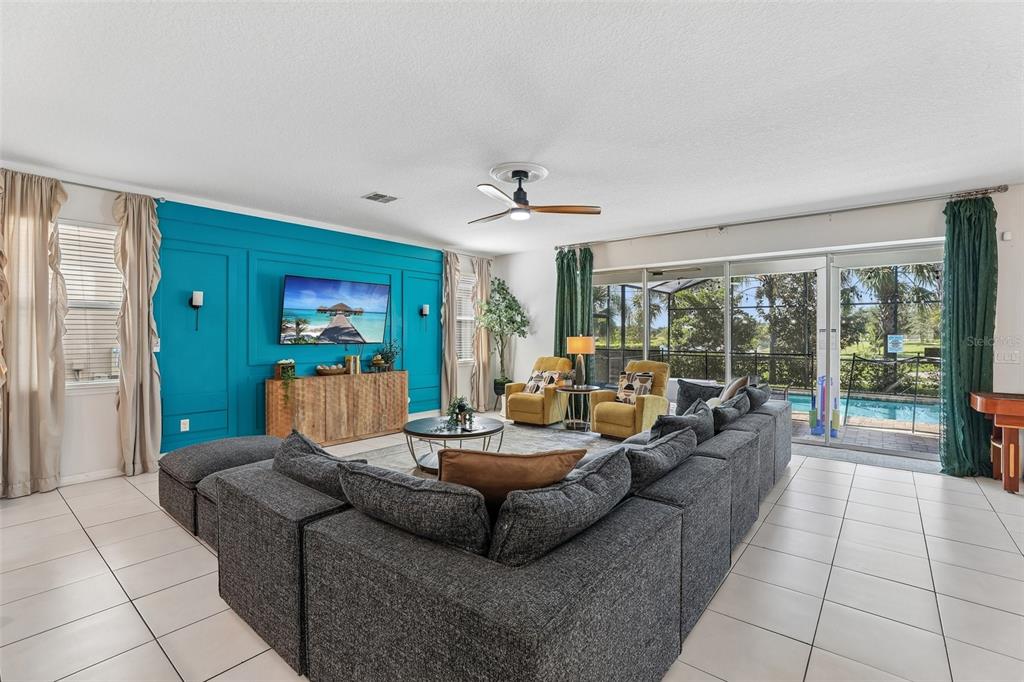 A living room features a blue accent wall, a large gray sectional, and sliding glass doors — 9001 SUNSHINE RIDGE LOOP, KISSIMMEE, FL