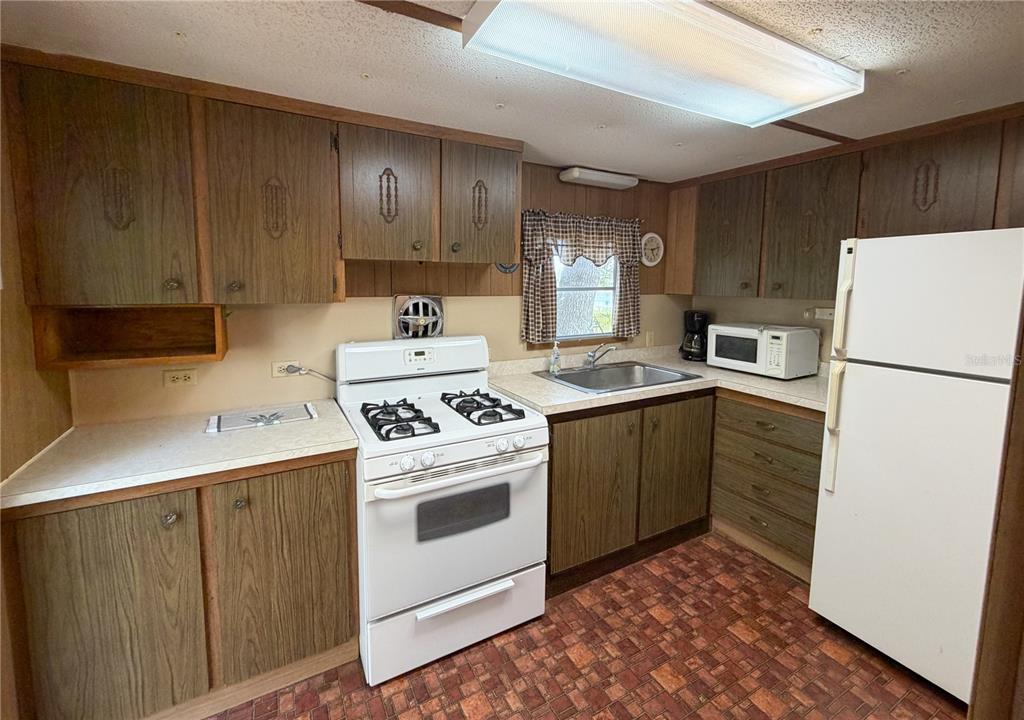 A kitchen features wood-grain cabinets, a white stove, a white refrigerator, and patterned vinyl flooring — 170 E COWPEN LAKE POINT ROAD, HAWTHORNE, FL