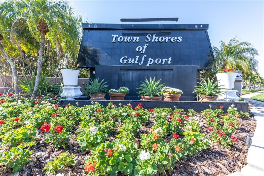 A black monument sign for Town Shores of Gulfport sits behind a colorful flower bed — 6020 SHORE BOULEVARD S UNIT 412, GULFPORT, FL