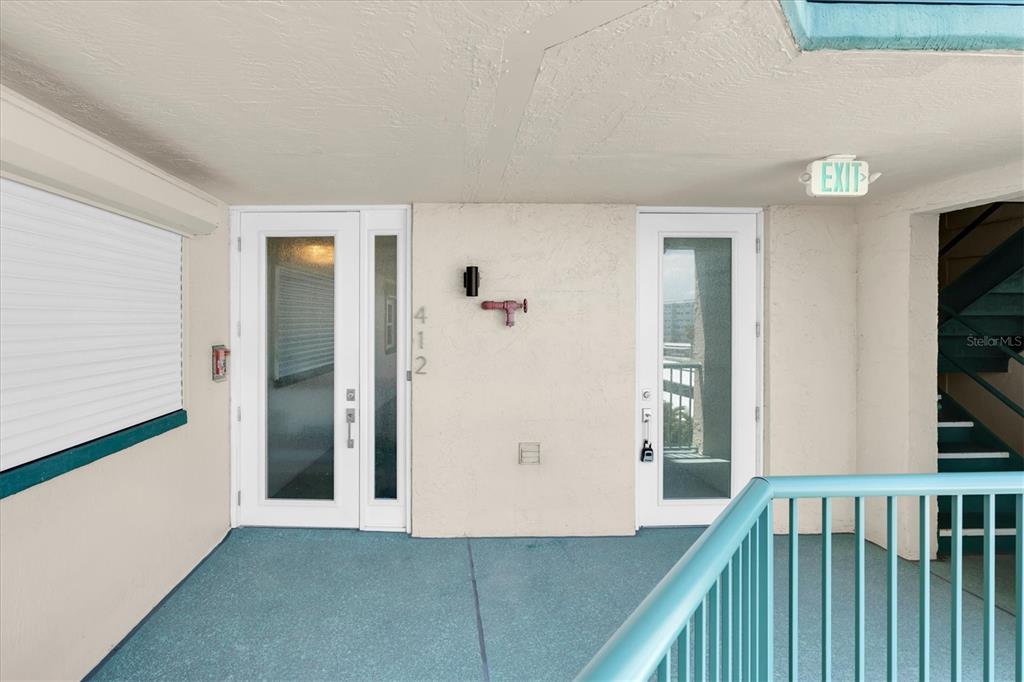 An exterior hallway features two white doors, a teal railing, and an exit sign — 6020 SHORE BOULEVARD S UNIT 412, GULFPORT, FL