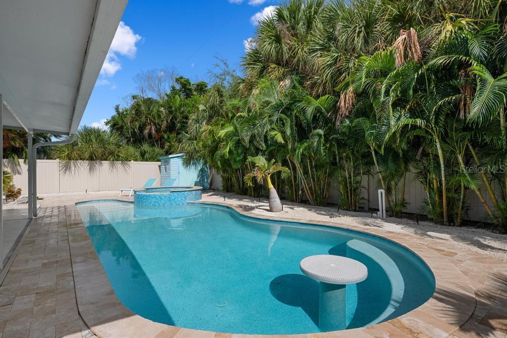 A swimming pool with a built-in table and spa sits in a landscaped backyard — 406 BAY PALMS DRIVE, HOLMES BEACH, FL
