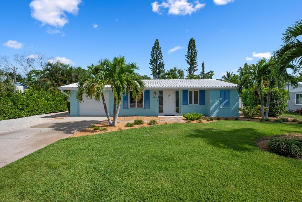 A light blue, single-story house with a white roof, garage, and palm trees in the yard — 406 BAY PALMS DRIVE, HOLMES BEACH, FL