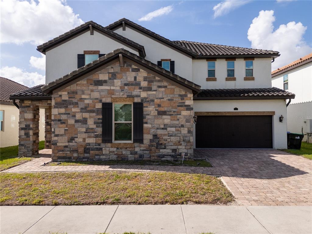 A two-story house features a stone facade, dark shutters, a tile roof, and a paved driveway — 17526 BLACK RAIL STREET, WINDERMERE, FL