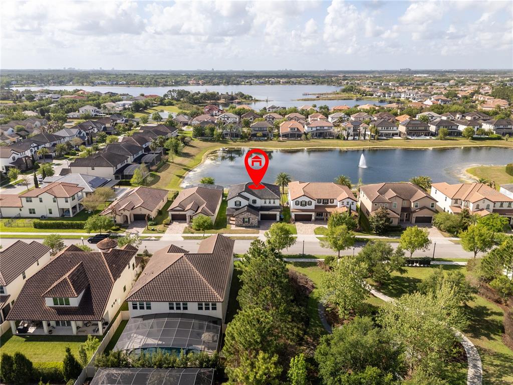 An aerial view shows a suburban neighborhood with houses surrounding a lake and fountain — 17526 BLACK RAIL STREET, WINDERMERE, FL
