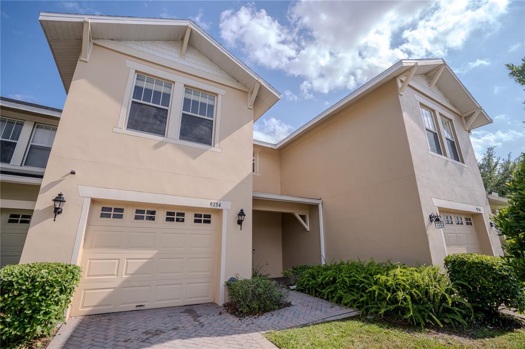A two-story townhouse with a beige stucco exterior, a single-car garage, and a paved driveway — 9734 TIRAMASU TRAIL, ORLANDO, FL