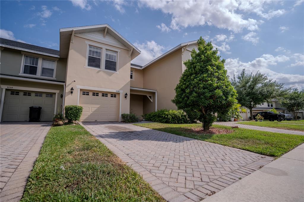 A two-story tan stucco townhouse features a single-car garage and a covered front entryway — 9734 TIRAMASU TRAIL, ORLANDO, FL