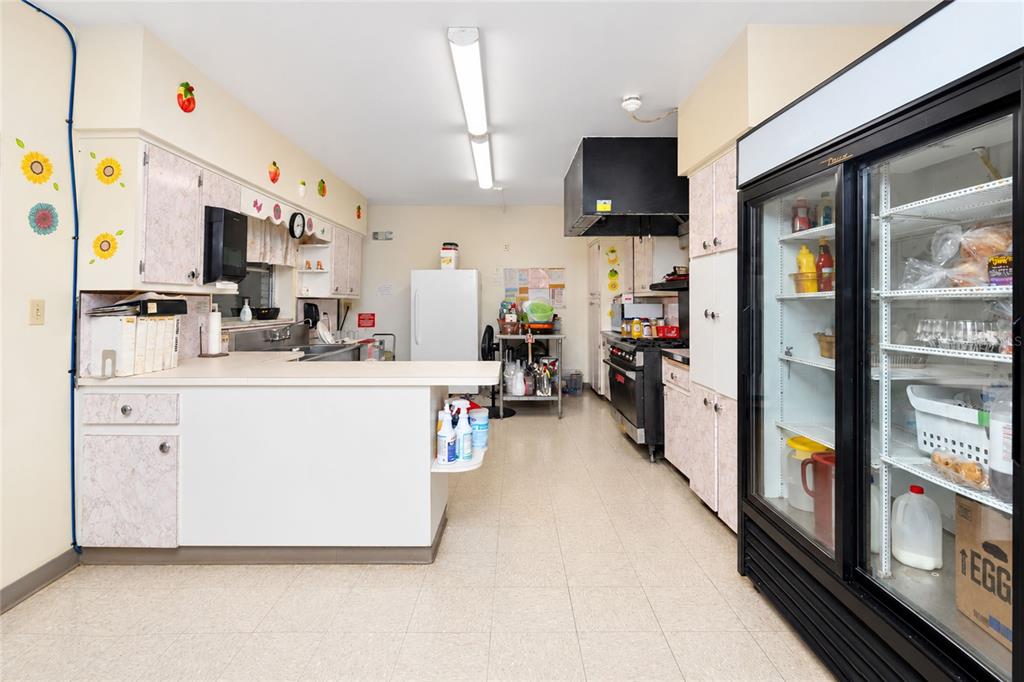 A commercial kitchen features white cabinetry, a large glass-door refrigerator, and a stainless steel stove — 24438 and 24450 HARBORVIEW ROAD, PORT CHARLOTTE, FL