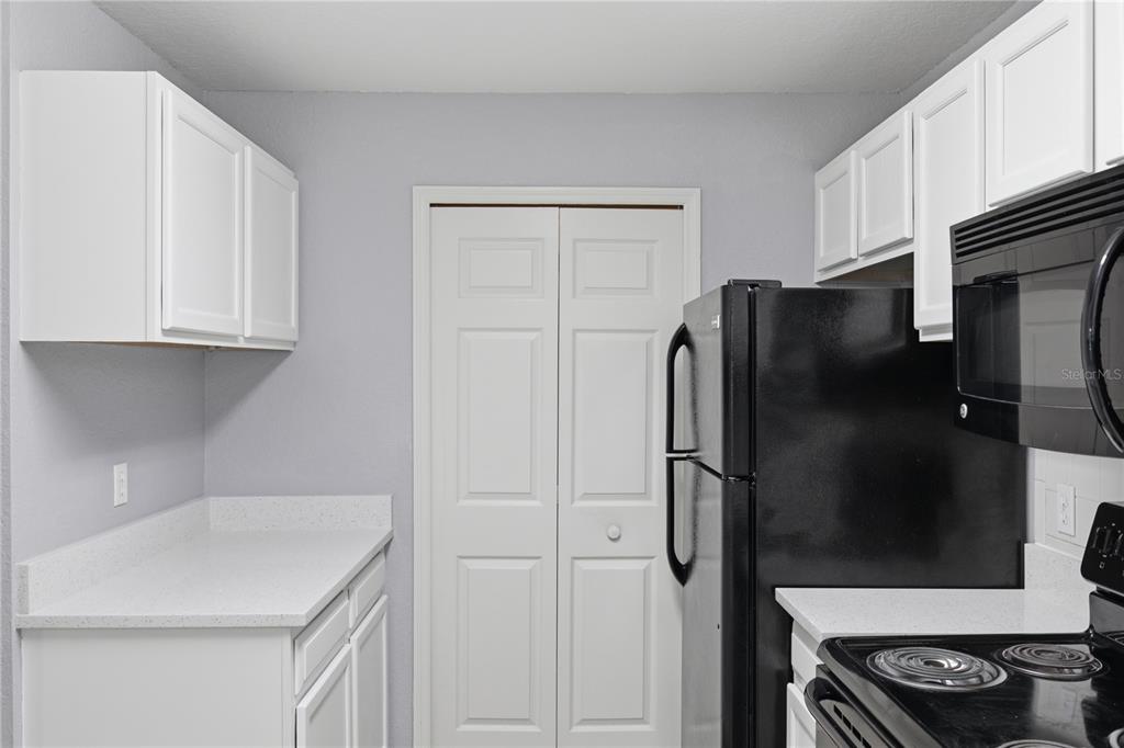 A kitchen features white cabinets, black appliances, a breakfast bar, and light-colored countertops — 7605 PISSARRO DRIVE UNIT 13204, ORLANDO, FL