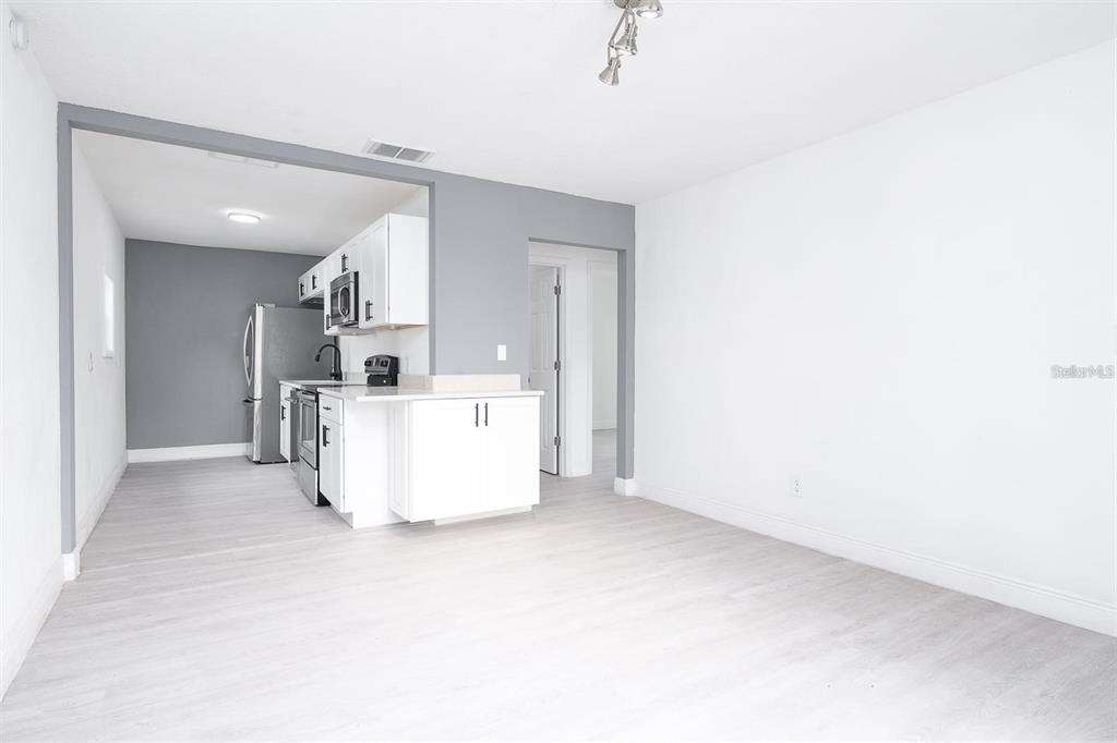 A kitchen with white cabinets and stainless steel appliances opens into a bright living area — 519 WILLIAMS STREET, MELBOURNE, FL