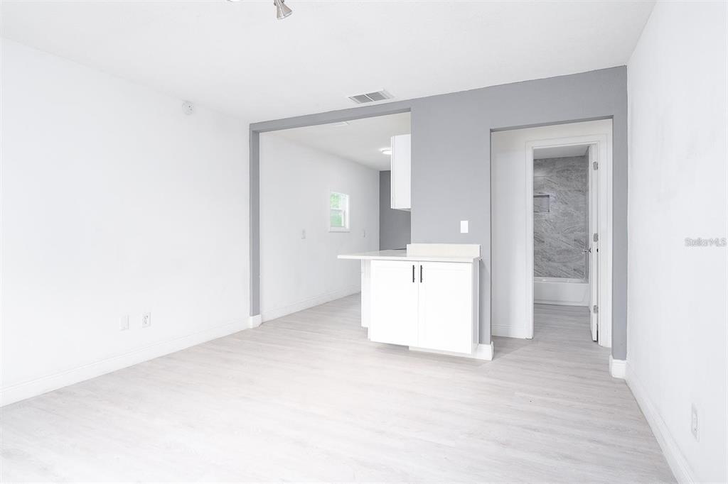 A living area with light wood-look flooring leads to a kitchen and a bathroom doorway — 519 WILLIAMS STREET, MELBOURNE, FL