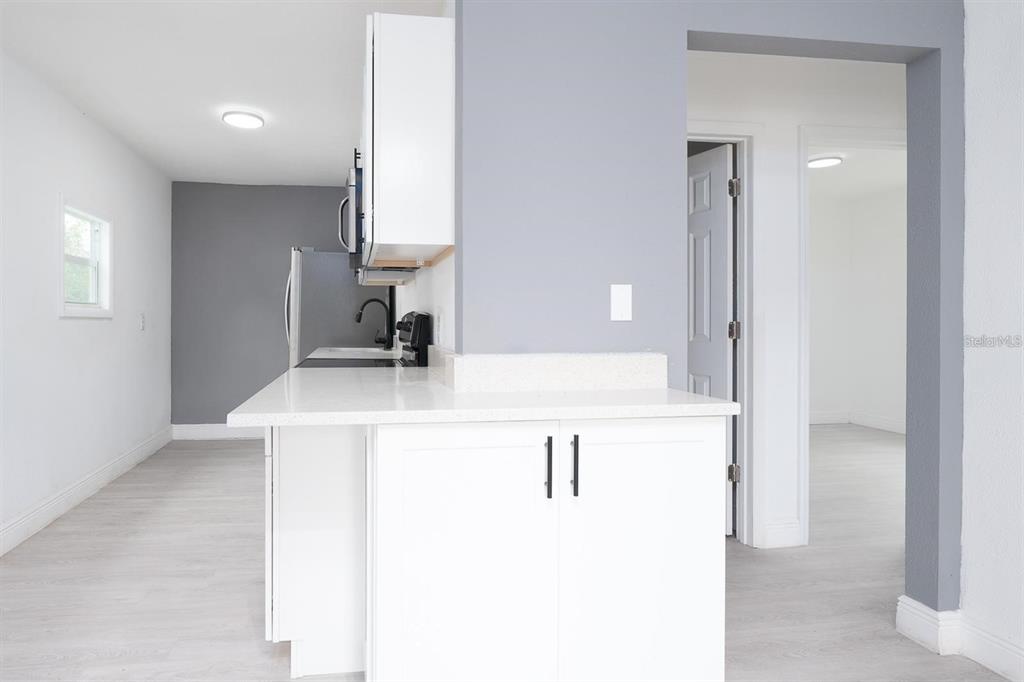 A kitchen with white cabinets and countertops opens to a hallway and adjacent room — 519 WILLIAMS STREET, MELBOURNE, FL