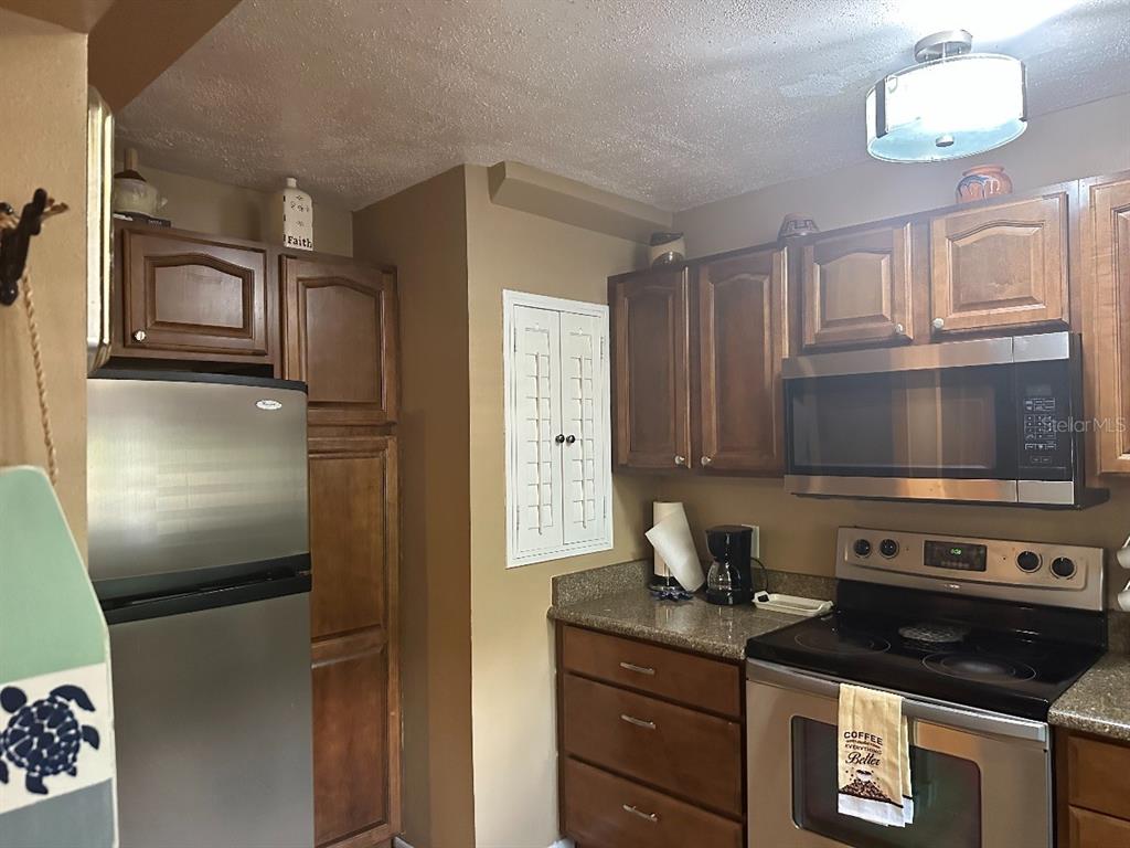 A kitchen features wood cabinets, stainless steel appliances, and a small white shuttered wall cabinet — 600 CRANES WAY UNIT 204, ALTAMONTE SPRINGS, FL