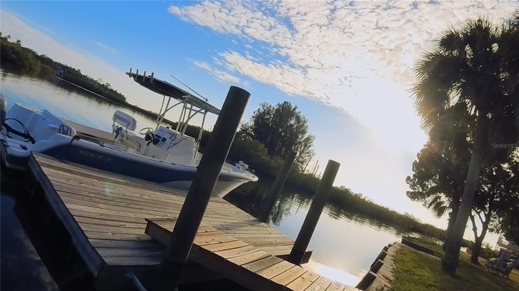 A boat is docked at a wooden pier along a waterway with palm trees nearby — 3044 SUNSET VISTA DRIVE, SPRING HILL, FL