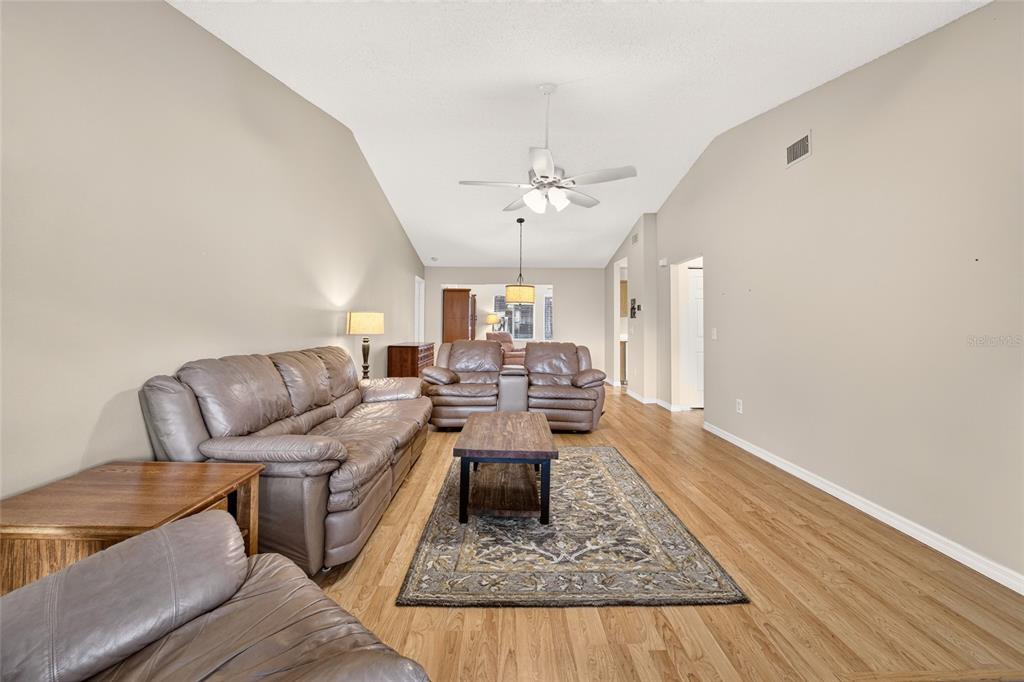 A living room features light wood flooring, tan walls, a vaulted ceiling, and leather furniture — 8661 SW 65TH TERRACE, OCALA, FL