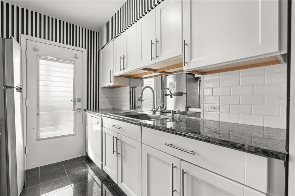 A white exterior walkway features a green door, a window, and a small bistro set — 1700 6TH STREET NW UNIT B24, WINTER HAVEN, FL