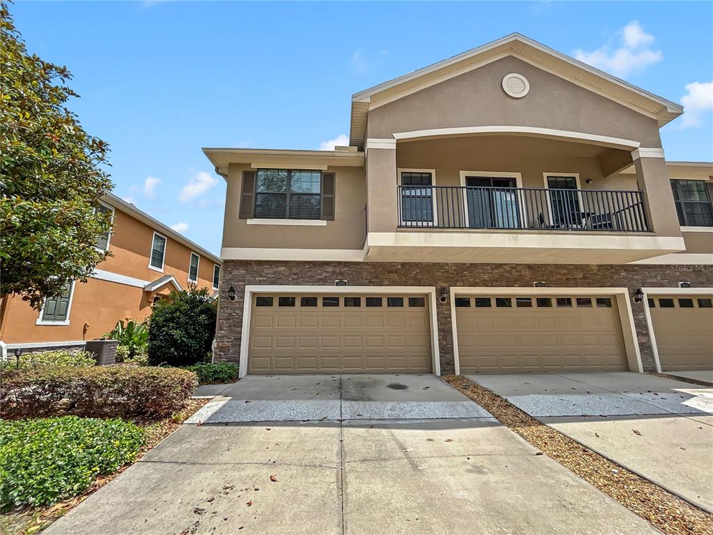 The exterior of a two-story townhouse features a stone facade, two garage doors, and a balcony — 16615 KINGLETSIDE COURT, LITHIA, FL