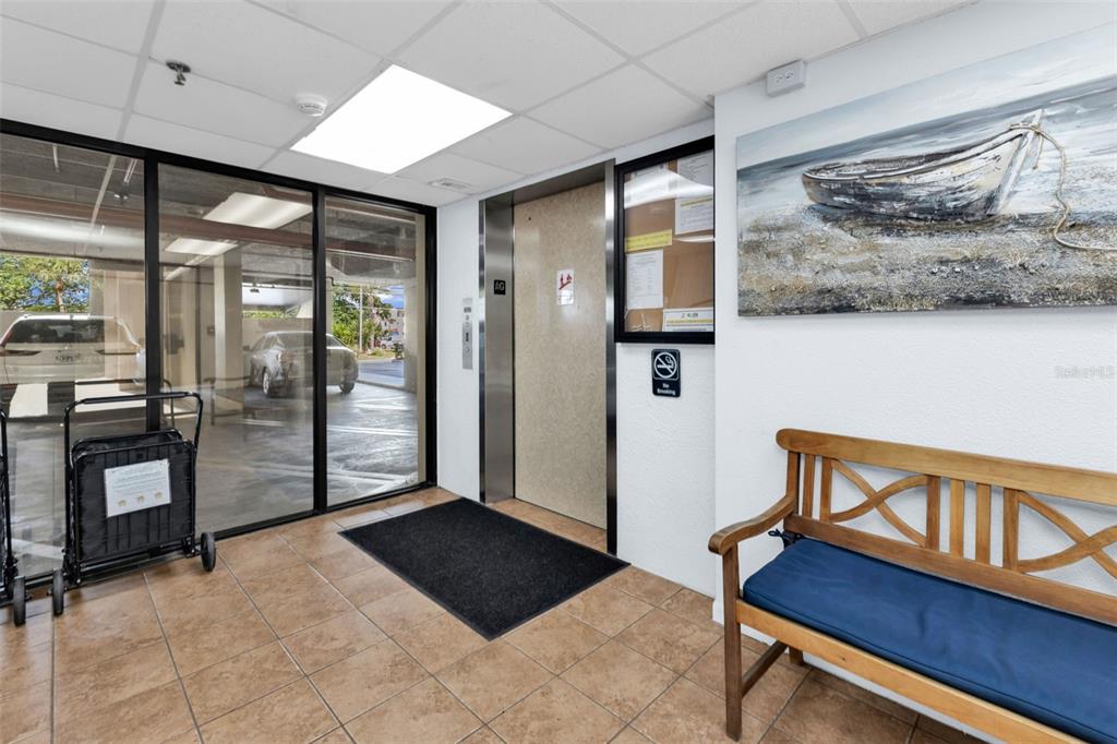A tiled elevator lobby features a wooden bench, a boat painting, and glass-walled exterior views — 21405 OLEAN BOULEVARD UNIT 528, PORT CHARLOTTE, FL
