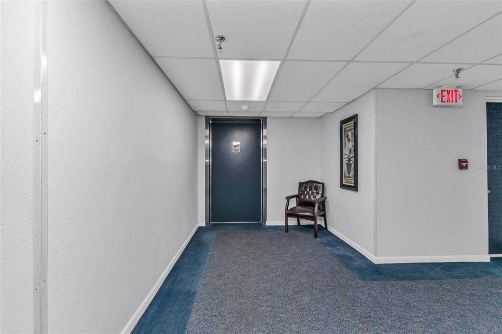 A hallway features a dark blue elevator door, a single leather chair, and blue carpeting — 21405 OLEAN BOULEVARD UNIT 528, PORT CHARLOTTE, FL