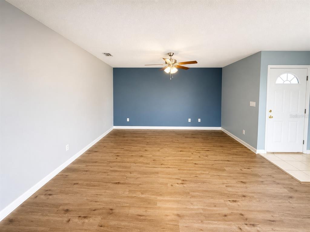 An empty living room features wood-look flooring, a blue accent wall, and a ceiling fan — 1013 APOLLO BEACH BOULEVARD UNIT 202, APOLLO BEACH, FL