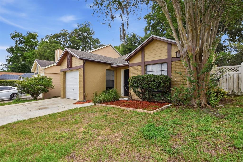 A tan single-story house with a white garage door, brick accents, and a front lawn — 1183 PIN OAK DRIVE, APOPKA, FL