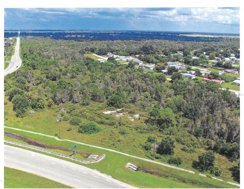 An aerial view shows a vacant, wooded lot adjacent to a highway and residential neighborhood — 27164 27176 27172 & KNOLLWOOD COURT, PUNTA GORDA, FL