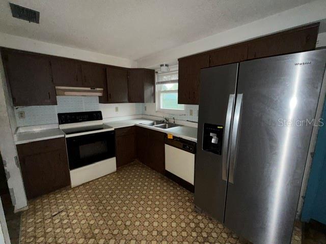 A kitchen features dark wood cabinets, a stainless steel refrigerator, and patterned linoleum flooring — 1050 BEACH LANE, WINTER HAVEN, FL