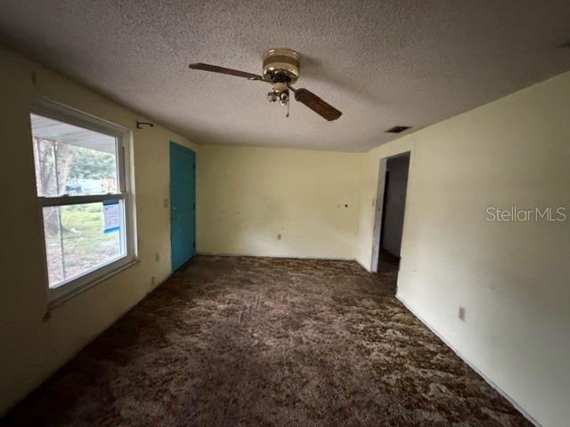 An empty room features brown patterned carpet, pale yellow walls, a ceiling fan, and a door — 1050 BEACH LANE, WINTER HAVEN, FL