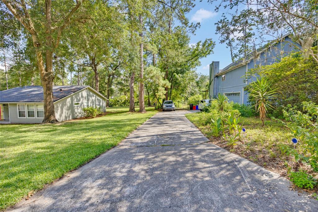 A concrete driveway leads between a single-story house and a two-story blue house — 7607 NW 42ND AVENUE, GAINESVILLE, FL