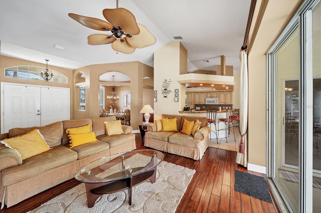 A living room with tan sofas, a glass coffee table, and a kitchen breakfast bar — 36 PINE VALLEY COURT, ROTONDA WEST, FL