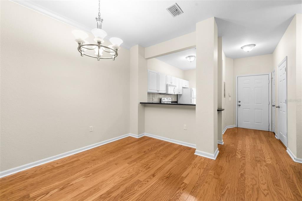 A dining area with hardwood floors, a chandelier, and a pass-through opening to the kitchen — 5007 NW 45TH ROAD UNIT 103, GAINESVILLE, FL