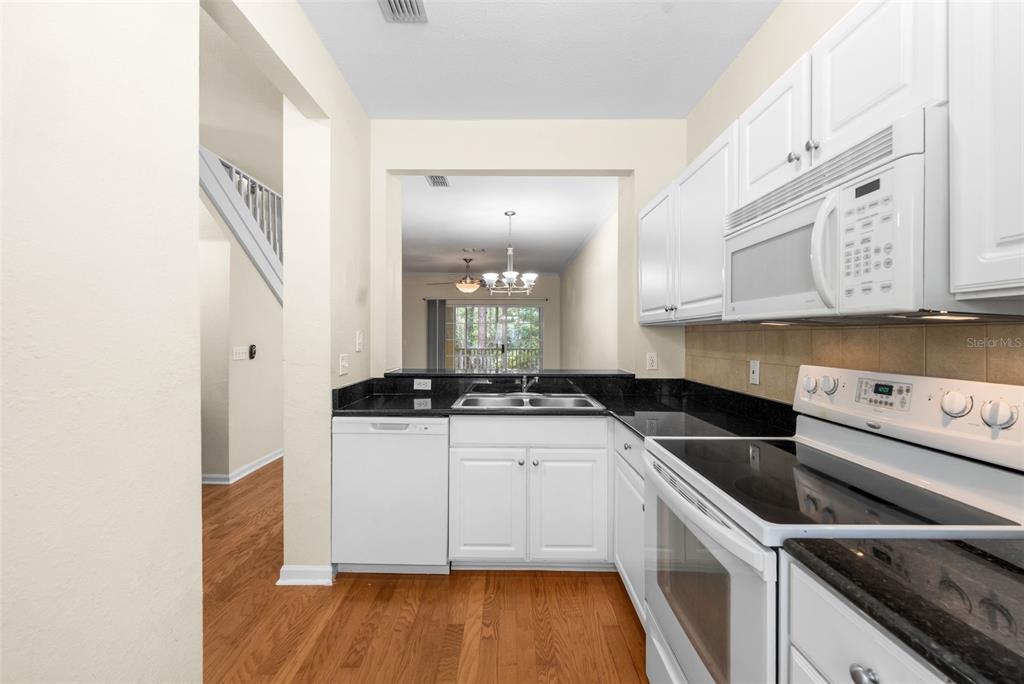 A kitchen with white cabinets, black countertops, and white appliances overlooks an adjacent dining area — 5007 NW 45TH ROAD UNIT 103, GAINESVILLE, FL