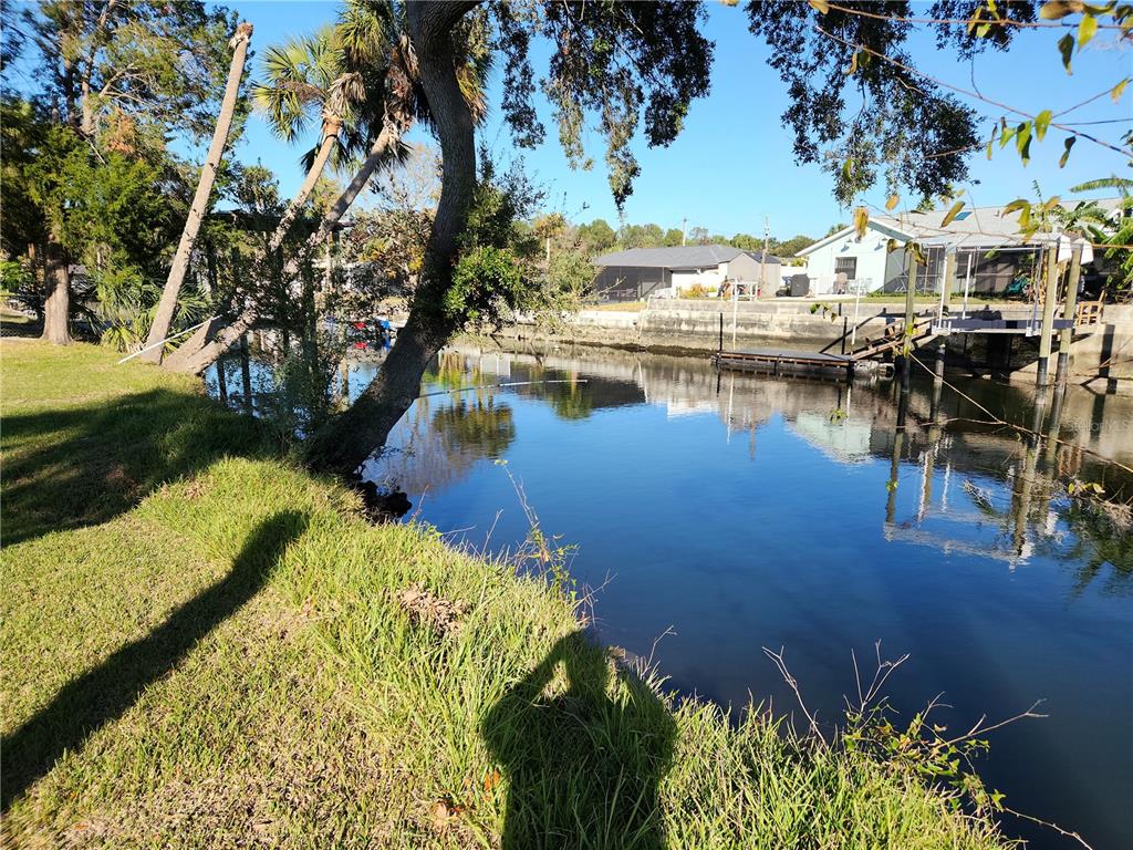 A grassy yard overlooks a narrow canal with a wooden dock and nearby residential houses — 3879 N SEMINOLE POINT, CRYSTAL RIVER, FL