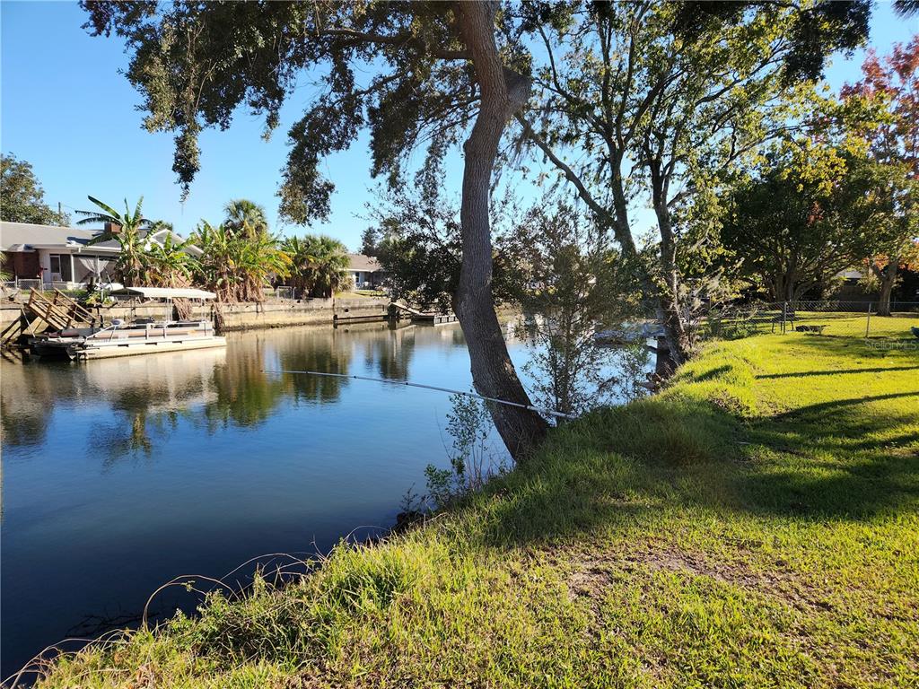 A grassy backyard overlooks a canal with a docked pontoon boat and mature trees — 3879 N SEMINOLE POINT, CRYSTAL RIVER, FL