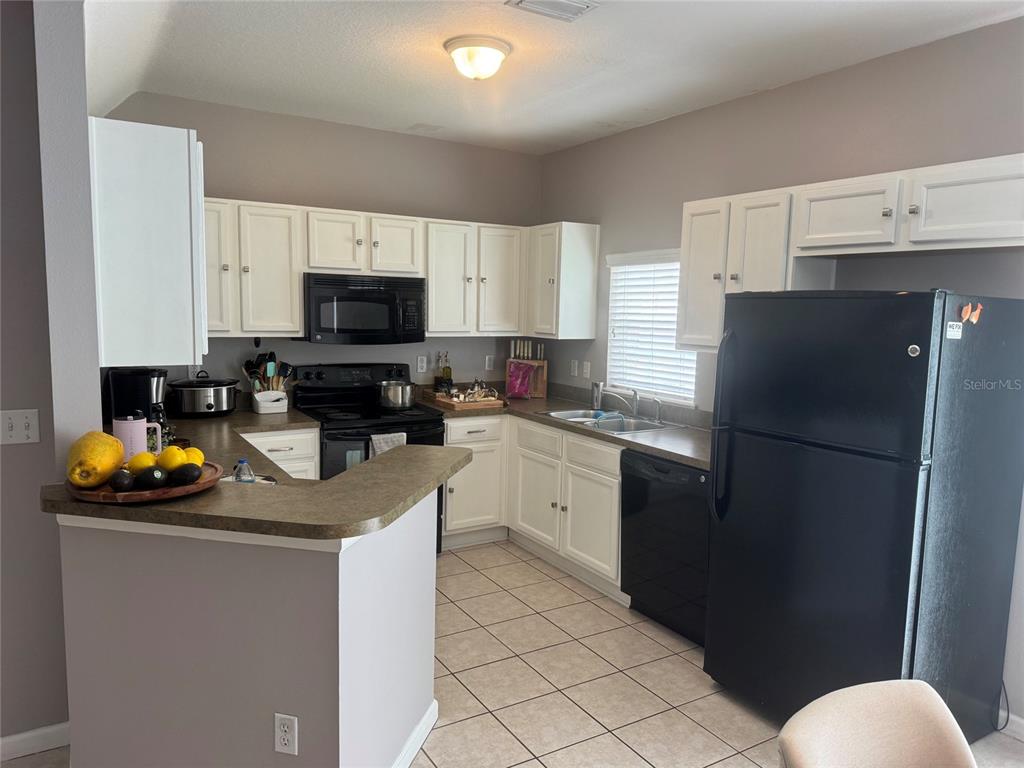 A kitchen features white cabinets, black appliances, a breakfast bar, and light-colored tile flooring — 319 SUMMER CLOUDS PLACE, BRANDON, FL